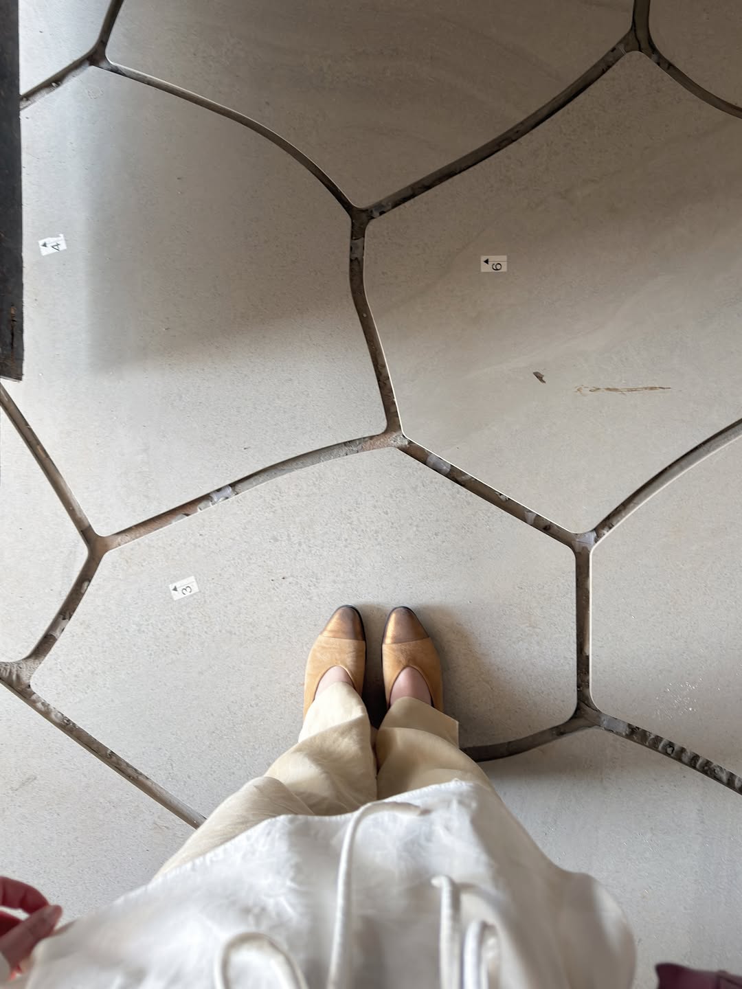 Registro de obra com peças de revestimento orgânicas e os pés da arquiteta sobre uma das placas.